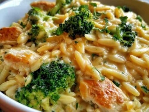 Creamy cheesy chicken broccoli orzo served in a large skillet with melted cheddar and fresh broccoli