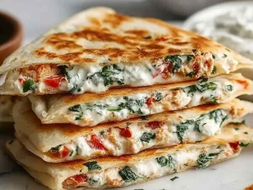 Cheesy Mediterranean quesadilla sliced into triangles on a wooden cutting board showing melted feta, mozzarella, spinach, and tomato filling