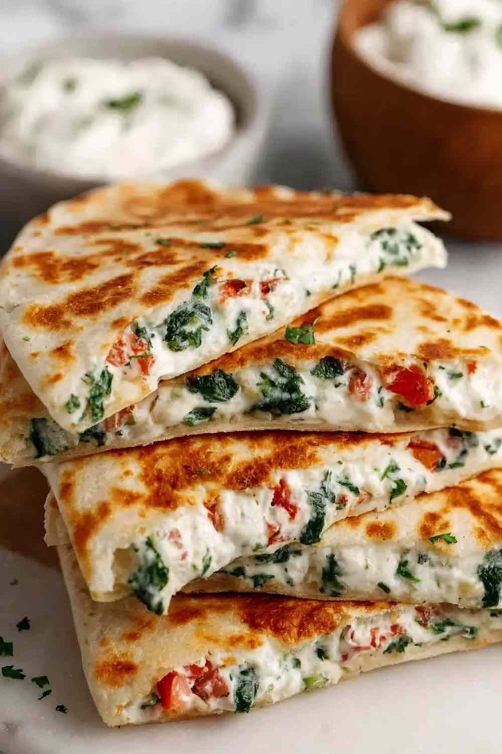 Cheesy Mediterranean quesadilla sliced into triangles on a wooden cutting board showing melted feta, mozzarella, spinach, and tomato filling