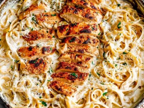 Creamy Chicken Alfredo recipe served in a large skillet with sliced chicken, fettuccine, and fresh parsley