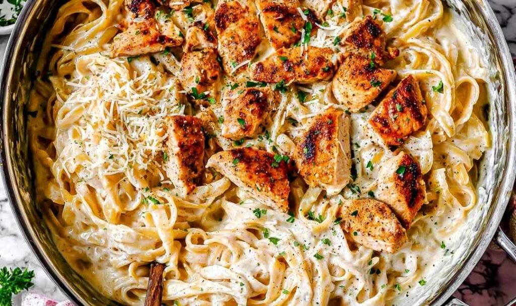 Creamy Chicken Alfredo recipe served in a large skillet with sliced chicken, fettuccine, and fresh parsley