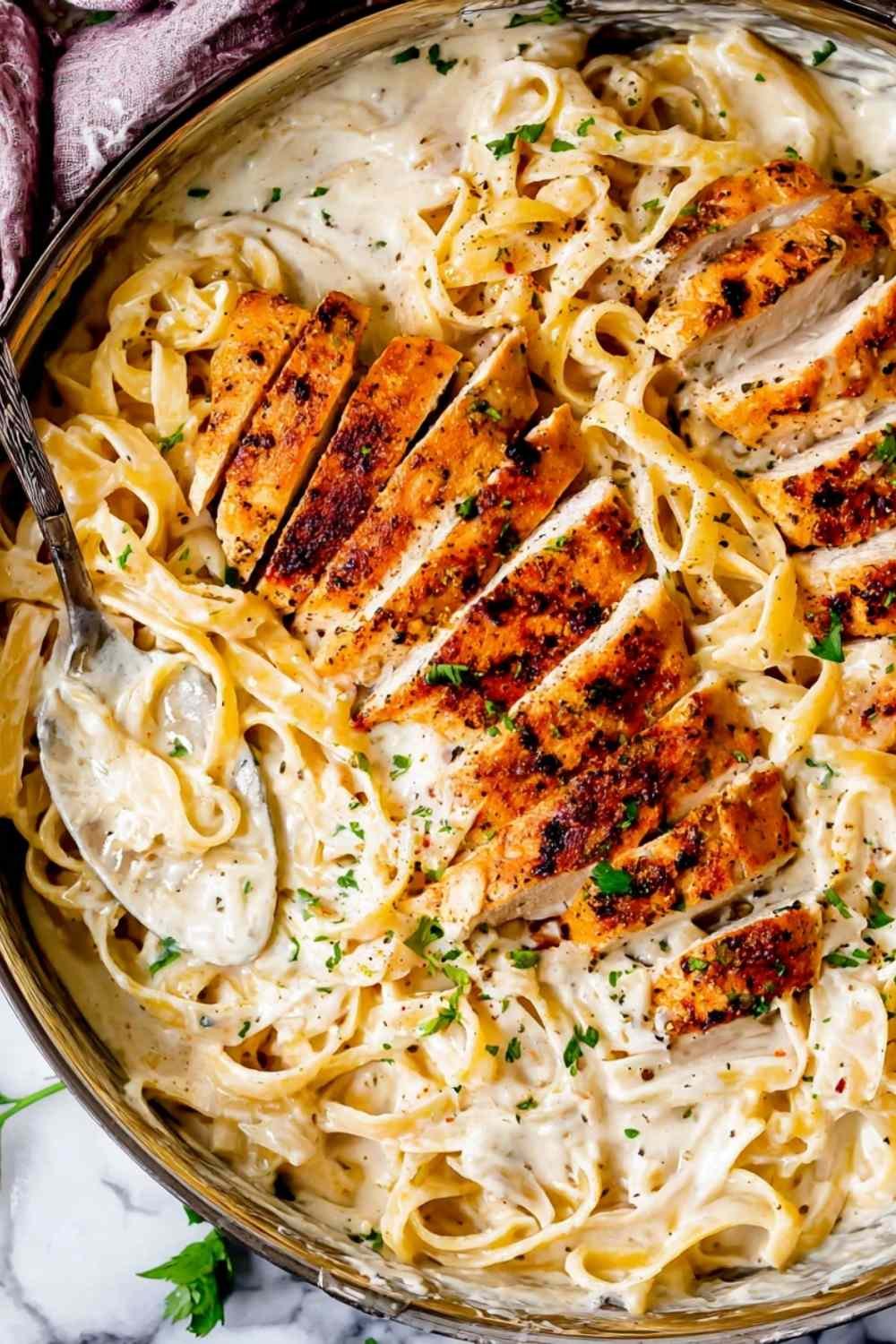 Creamy Chicken Alfredo recipe served in a large skillet with sliced chicken, fettuccine, and fresh parsley