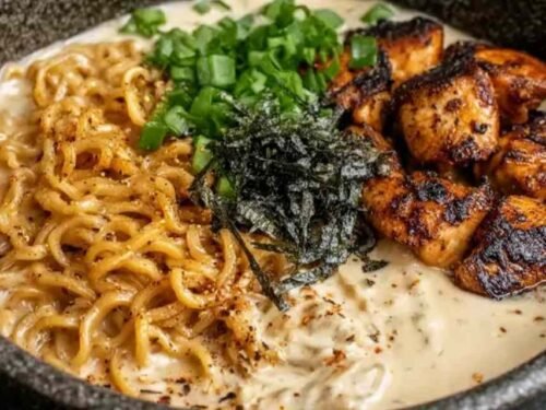 A bowl of chicken ramen with creamy garlic sauce topped with green onions, served hot in a white bowl