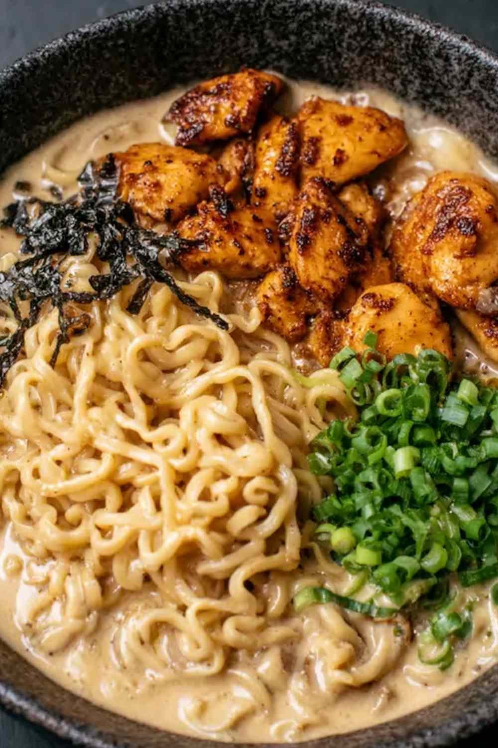 A bowl of chicken ramen with creamy garlic sauce topped with green onions, served hot in a white bowl