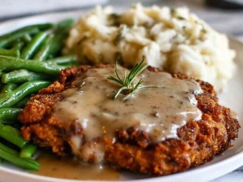 Crispy homestyle chicken fried steak recipe served on a plate and smothered in creamy peppery white gravy