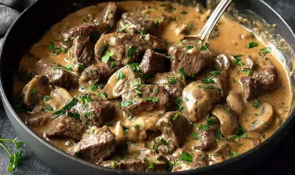 Gordon Ramsay's beef stroganoff served over buttered egg noodles with fresh chives in a cast iron skillet