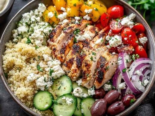 Greek Chicken Quinoa Bowl topped with grilled chicken strips, diced cucumber, cherry tomatoes, avocado, feta, and olives