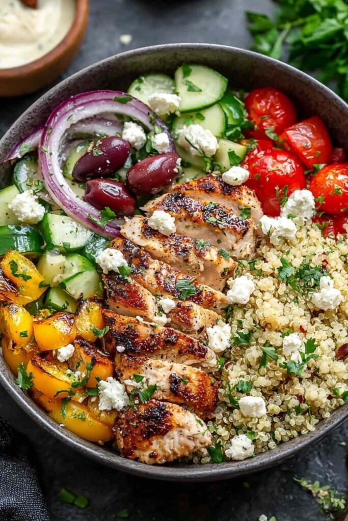 Greek Chicken Quinoa Bowl topped with grilled chicken strips, diced cucumber, cherry tomatoes, avocado, feta, and olives
