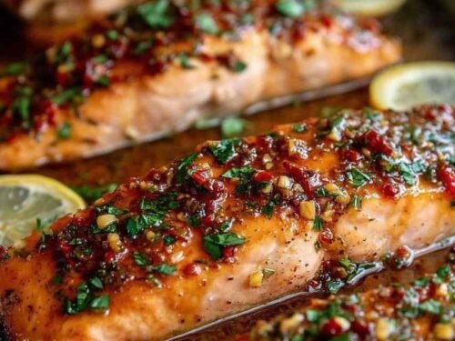 Honey garlic butter baked salmon fillets on a foil-lined baking tray with lemon slices and a golden caramelized glaze