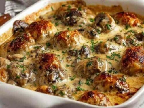 Keto garlic mushroom chicken casserole with golden melted cheese and fresh parsley in a white baking dish