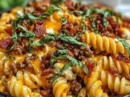 Loaded beef bacon cheeseburger pasta served in a white bowl topped with melted cheddar cheese and crispy bacon