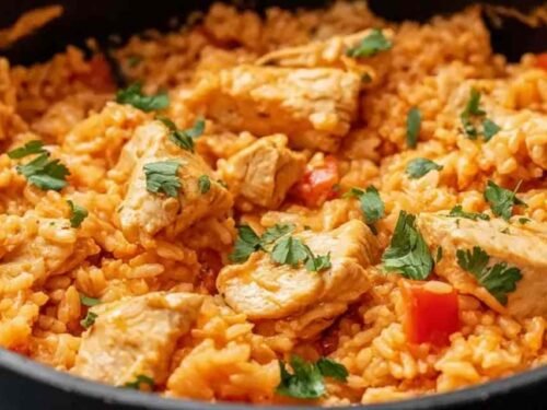 One pot queso chicken and rice served in a large skillet topped with fresh cilantro and sliced jalapenos