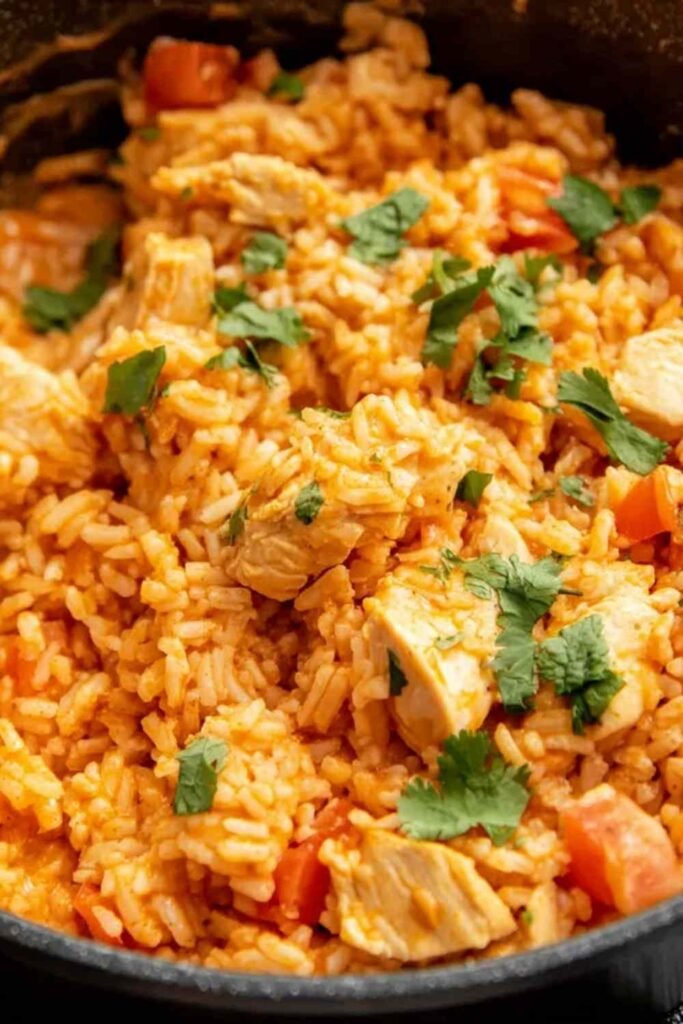 One pot queso chicken and rice served in a large skillet topped with fresh cilantro and sliced jalapenos