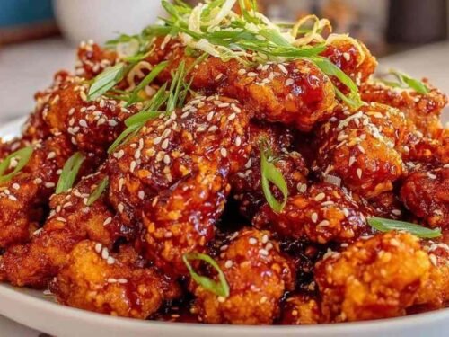 Crispy orange chicken recipe pieces coated in sticky orange sauce and topped with sesame seeds and fresh green onions