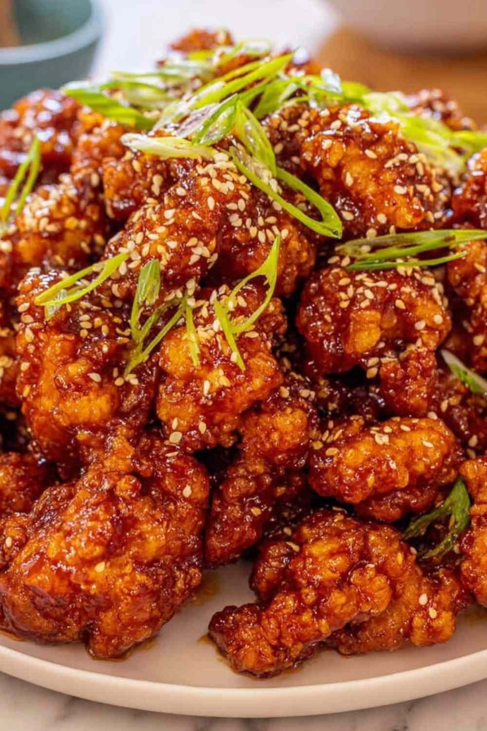 Crispy orange chicken recipe pieces coated in sticky orange sauce and topped with sesame seeds and fresh green onions