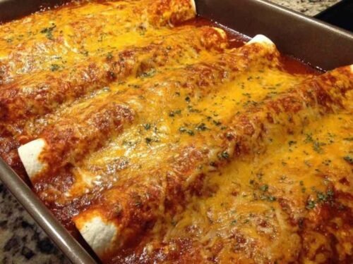 Queso Chicken Enchiladas baking in a glass dish with melted cheese