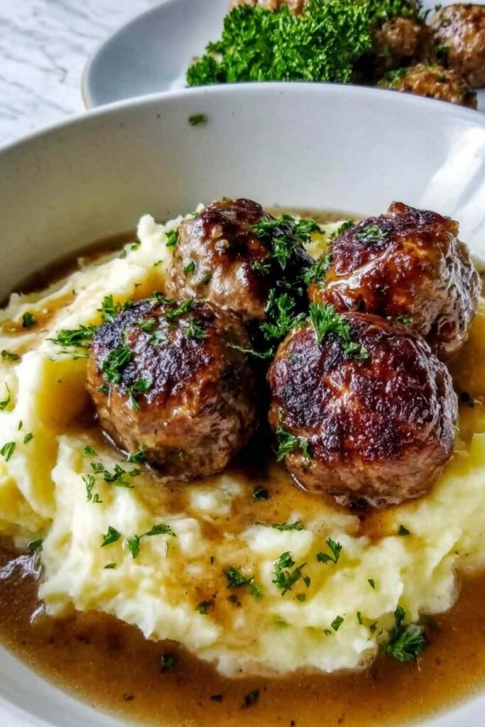 Salisbury Steak Meatballs with gravy served over garlic mashed potatoes on a white plate