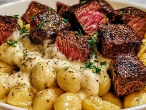 Steak bites and shell pasta in garlic butter Alfredo sauce served in a white bowl garnished with fresh parsley