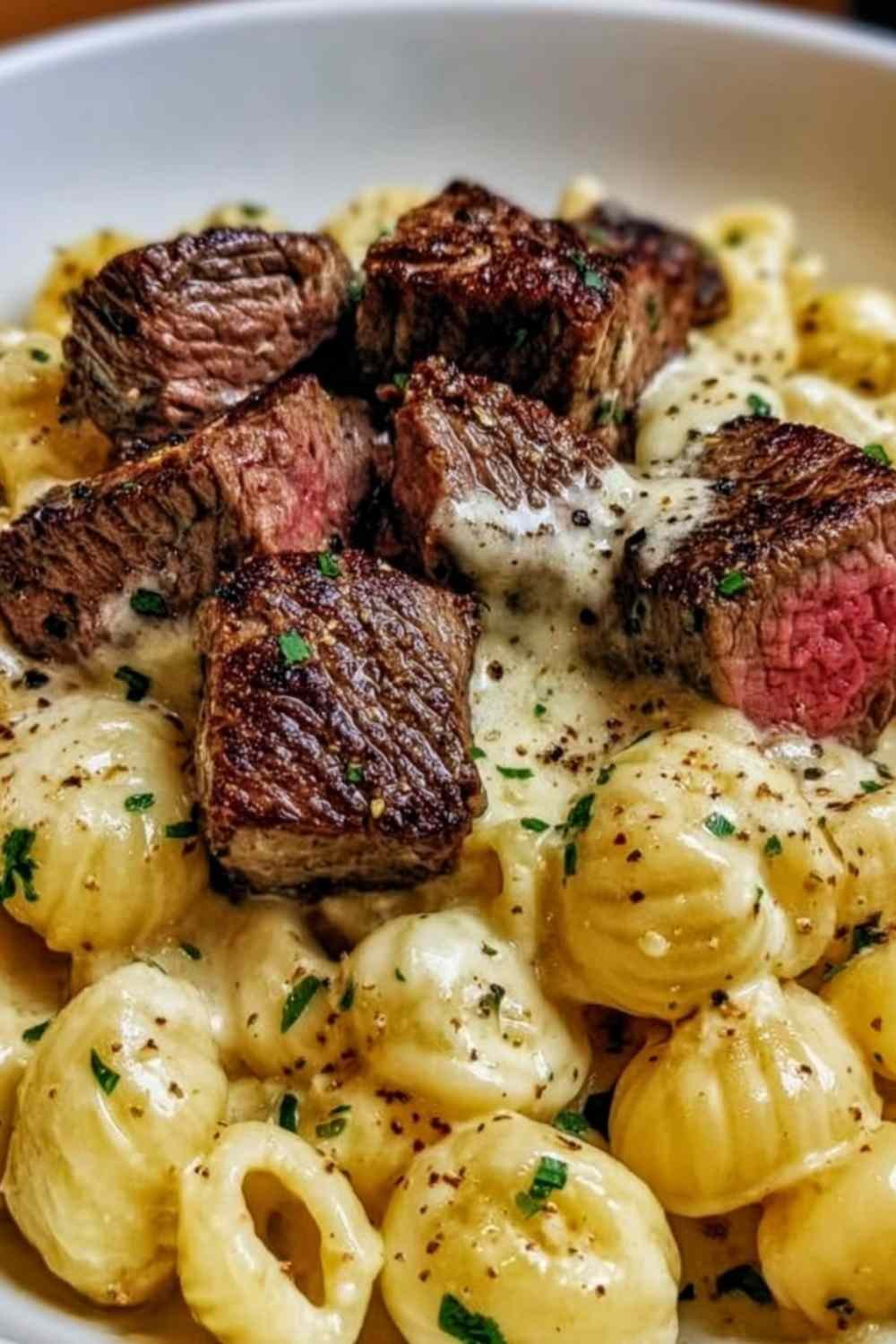 Steak bites and shell pasta in garlic butter Alfredo sauce served in a white bowl garnished with fresh parsley