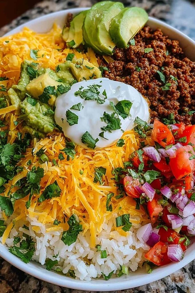 Fresh ingredients for a Taco Rice Bowl including ground meat, rice, and vegetables.