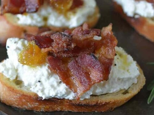 Bacon ricotta crostini topped with crispy bacon crumbles and honey drizzle on a rustic wooden board
