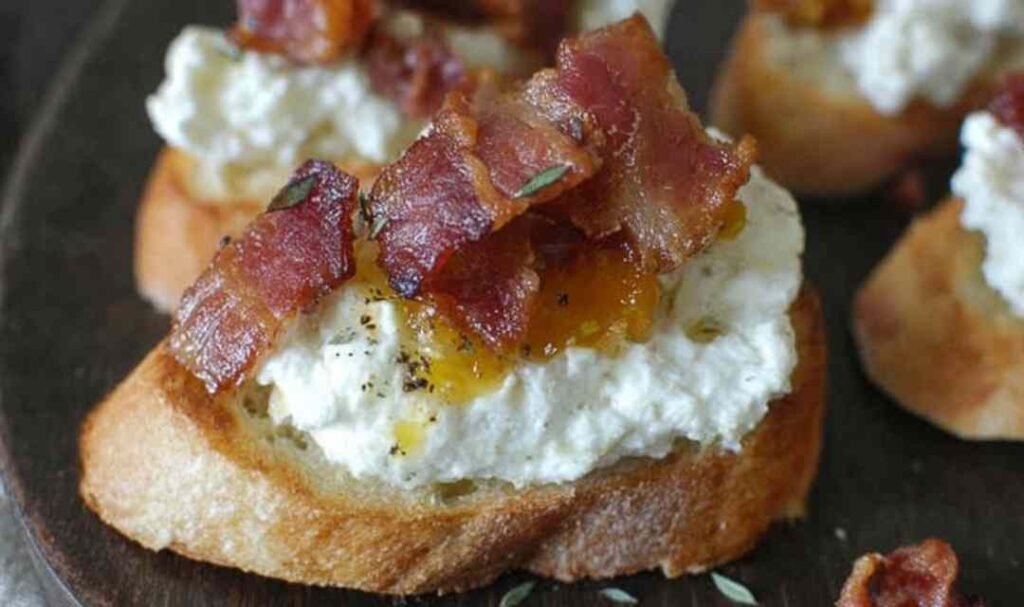 Bacon ricotta crostini topped with crispy bacon crumbles and honey drizzle on a rustic wooden board