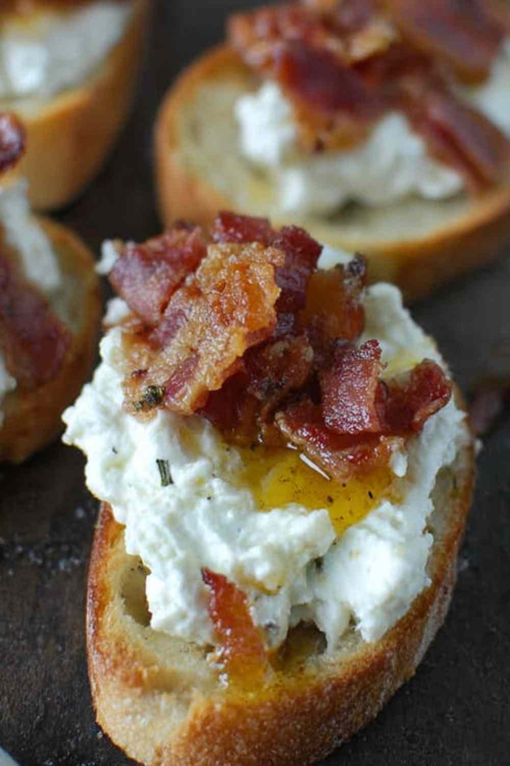 Bacon ricotta crostini topped with crispy bacon crumbles and honey drizzle on a rustic wooden board