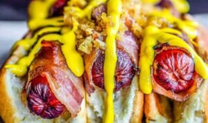 Bacon wrapped hot dogs grilling over low heat with crispy golden bacon on an outdoor grill
