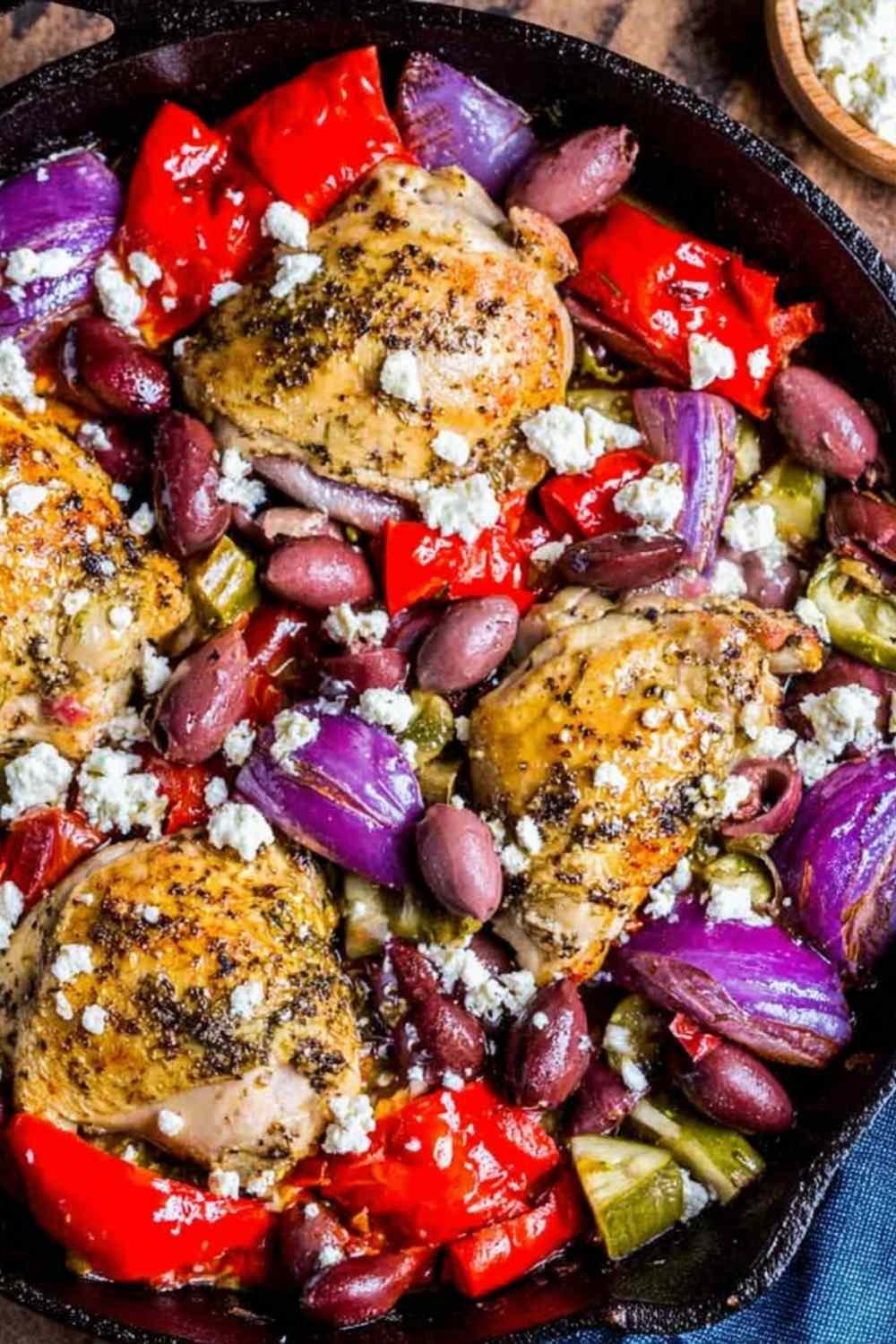 Greek chicken with veggies in a cast iron skillet topped with feta cheese and Kalamata olives