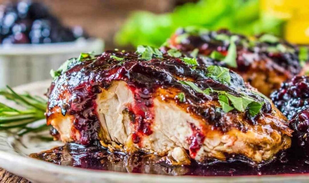 Blackberry balsamic glazed chicken breasts served on a white plate with fresh blackberries and balsamic glaze