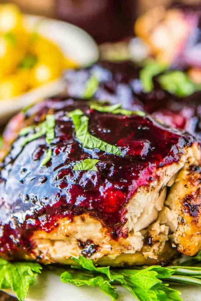 Blackberry balsamic glazed chicken breasts served on a white plate with fresh blackberries and balsamic glaze