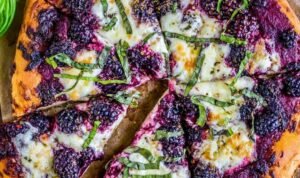 Blackberry ricotta pizza with basil on parchment paper fresh out of the oven with golden melted cheese and whole blackberries