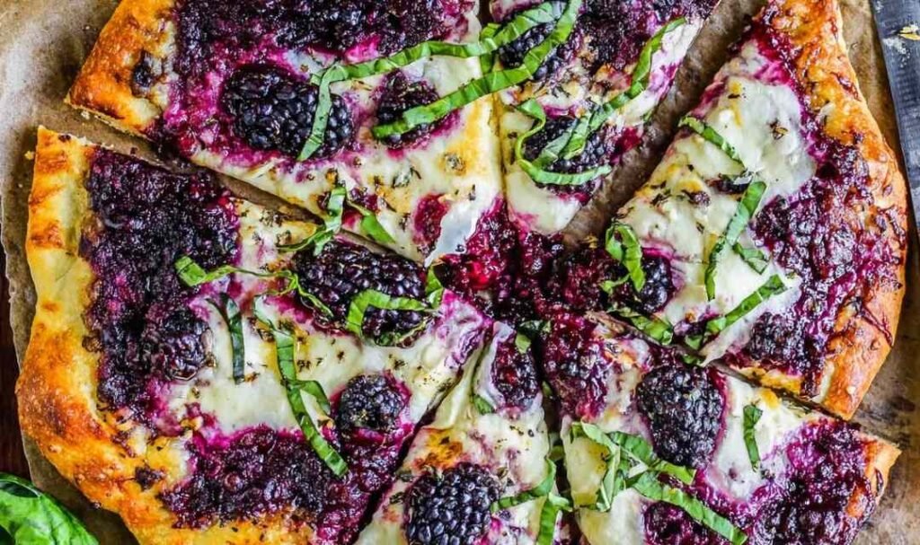 Blackberry ricotta pizza with basil on parchment paper fresh out of the oven with golden melted cheese and whole blackberries