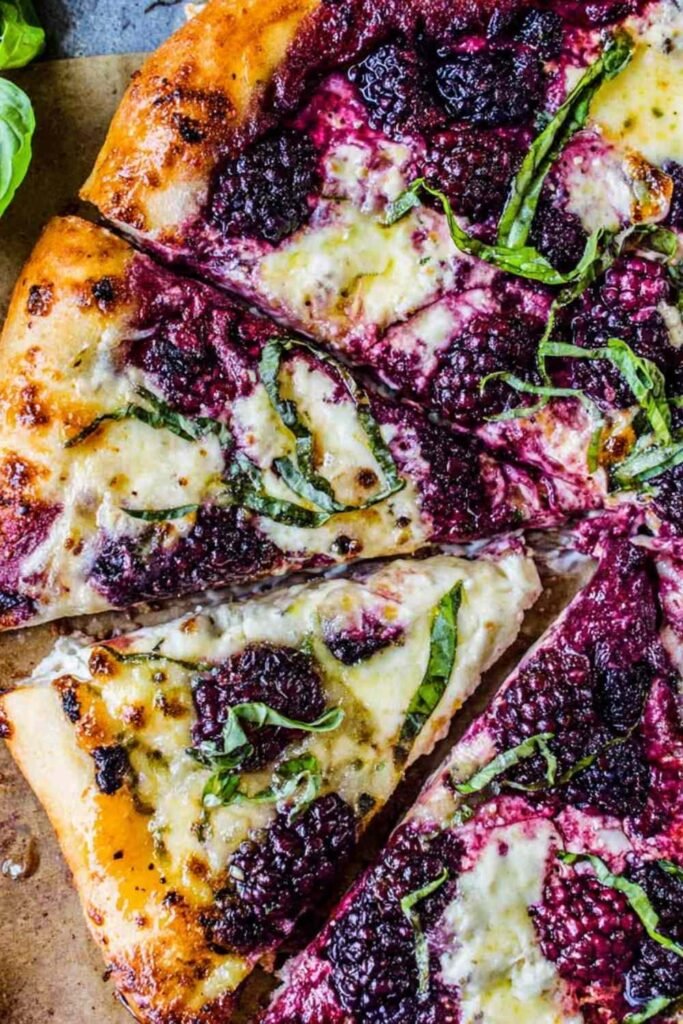 Blackberry ricotta pizza with basil on parchment paper fresh out of the oven with golden melted cheese and whole blackberries