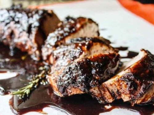Sliced brown sugar balsamic pork tenderloin crock pot recipe on a white serving platter with sticky caramelized glaze