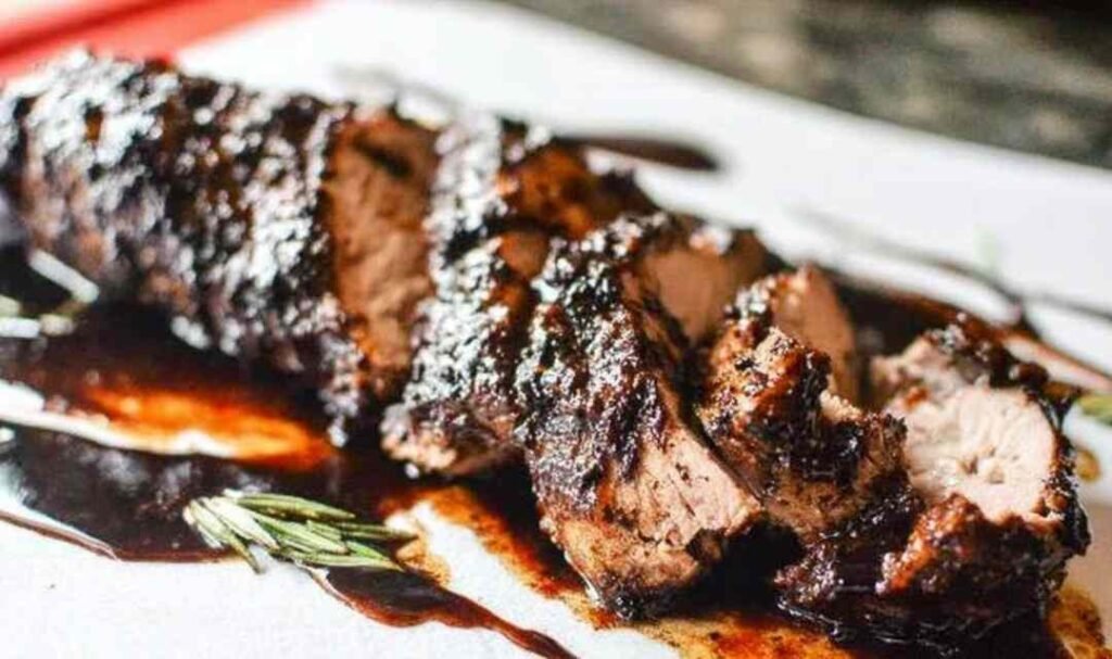 Sliced brown sugar balsamic pork tenderloin crock pot recipe on a white serving platter with sticky caramelized glaze