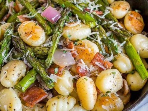 Brown butter gnocchi with asparagus and prosciutto in a cast iron skillet topped with freshly grated Parmesan cheese