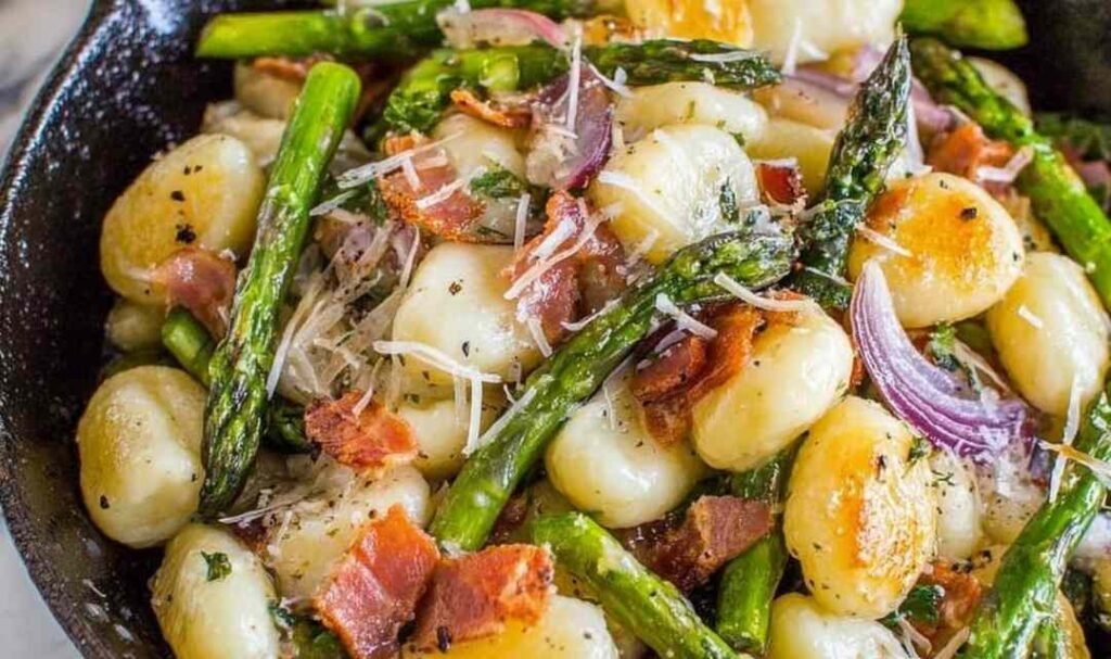 Brown butter gnocchi with asparagus and prosciutto in a cast iron skillet topped with freshly grated Parmesan cheese