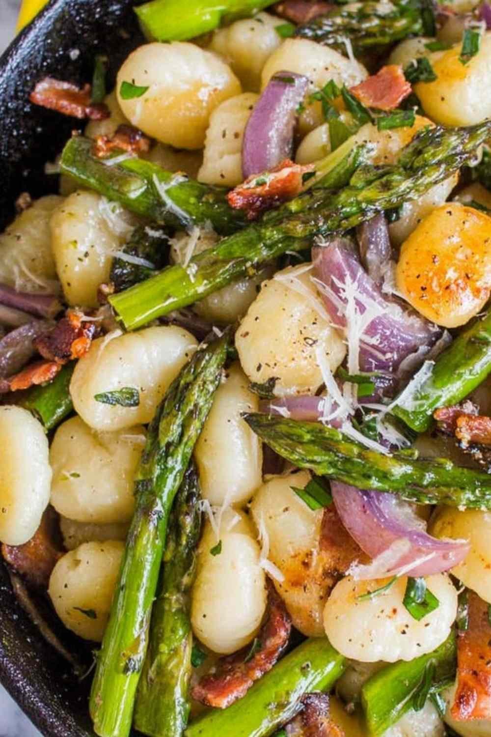 Brown butter gnocchi with asparagus and prosciutto in a cast iron skillet topped with freshly grated Parmesan cheese