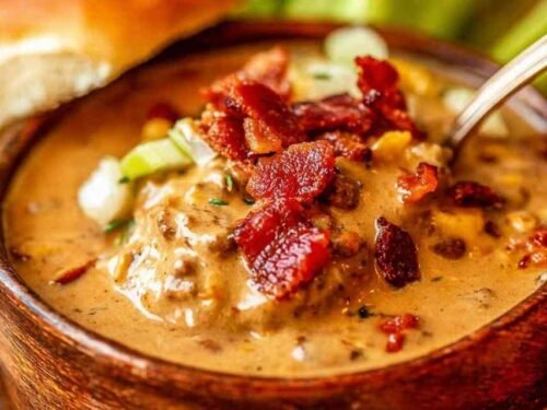 Bowl of cheeseburger soup topped with bacon and pickles.