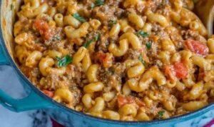 A bowl of homemade chili mac and cheese topped with shredded cheddar, sour cream, and green onions