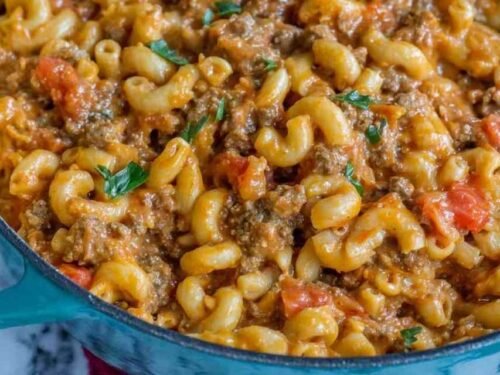 A bowl of homemade chili mac and cheese topped with shredded cheddar, sour cream, and green onions