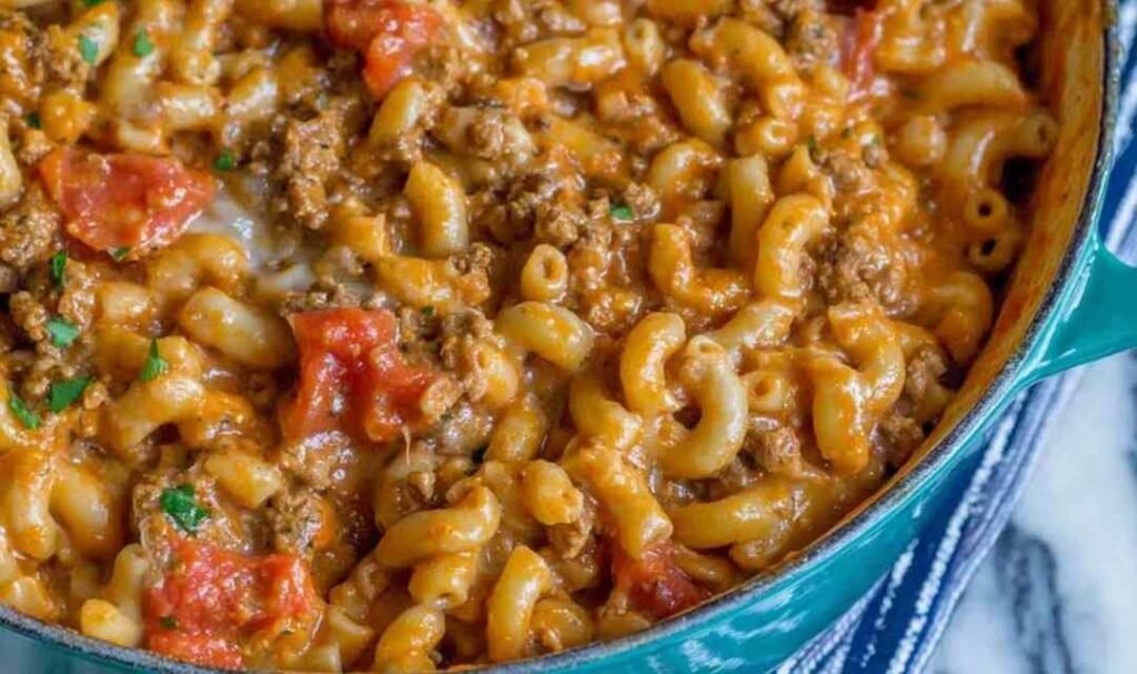 A bowl of homemade chili mac and cheese topped with shredded cheddar, sour cream, and green onions