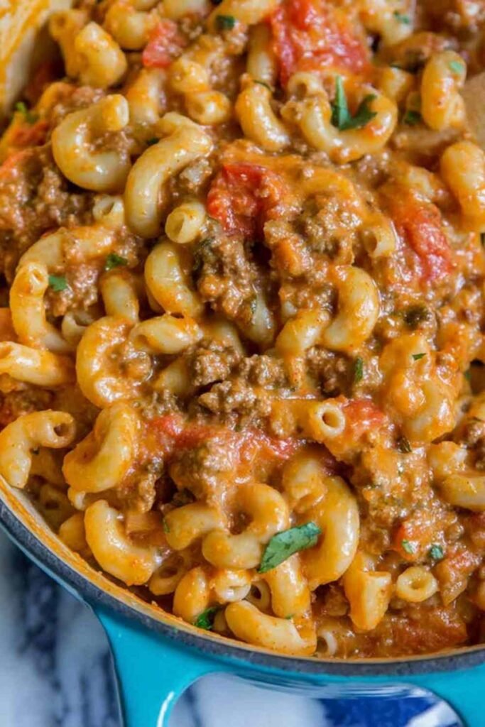 A bowl of homemade chili mac and cheese topped with shredded cheddar, sour cream, and green onions