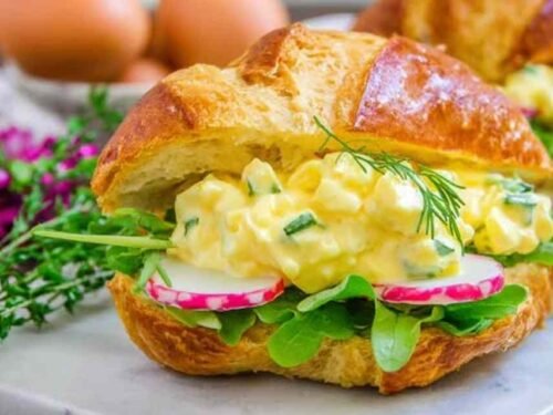 Classic egg salad sandwich on toasted whole grain bread with fresh chives on top served on a wooden board