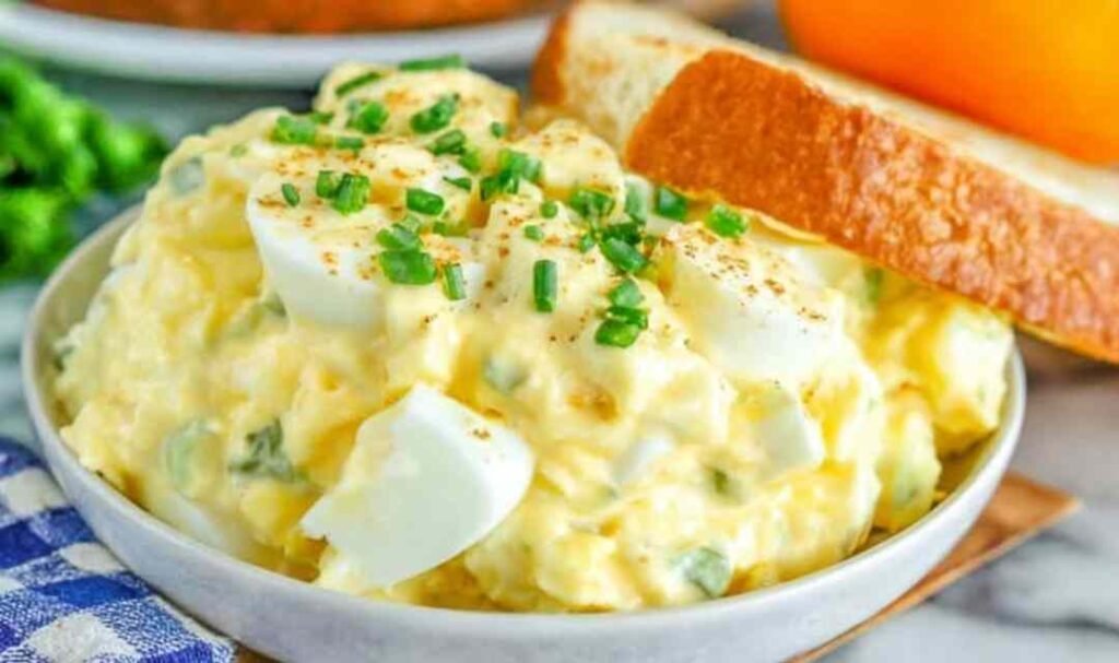 Classic egg salad sandwich on toasted whole grain bread with fresh chives on top served on a wooden board