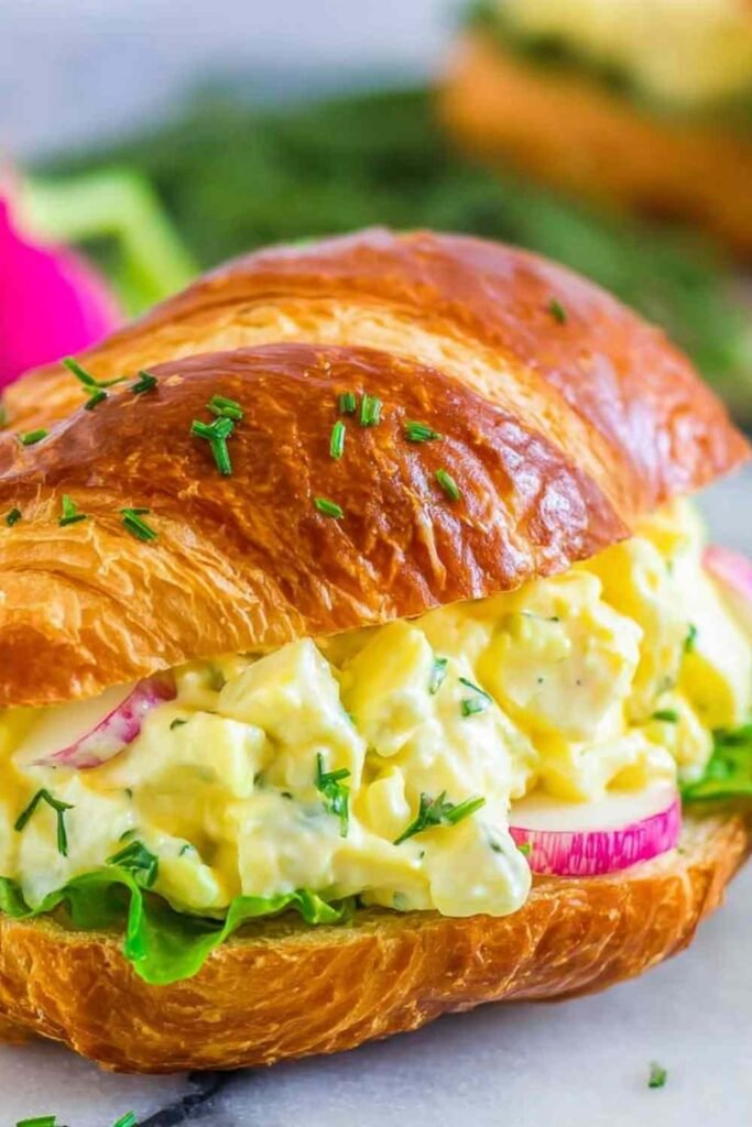 Classic egg salad sandwich on toasted whole grain bread with fresh chives on top served on a wooden board