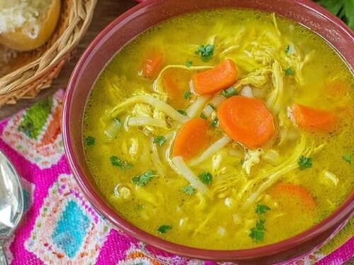 A bowl of creamy mulligatawny soup topped with avocado slices, fresh cilantro, and lime wedges on a wooden table