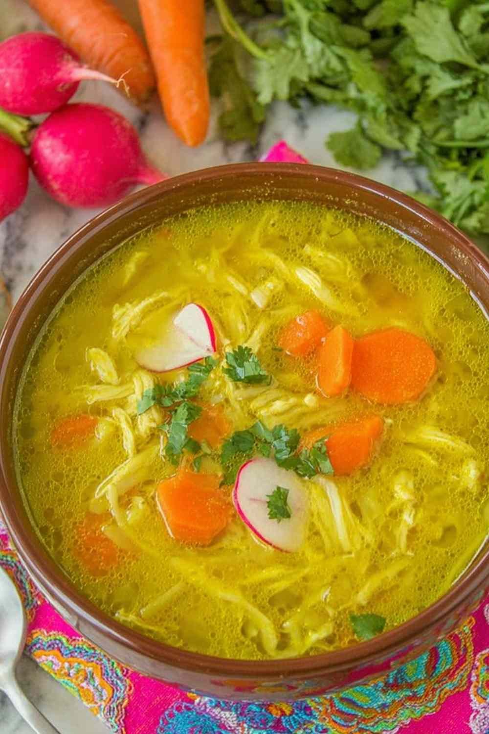 A bowl of creamy mulligatawny soup topped with avocado slices, fresh cilantro, and lime wedges on a wooden table