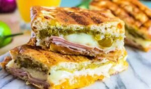 Ingredients for Cuban Sandwiches including ham, pork, pickles, and Swiss cheese on a cutting board.